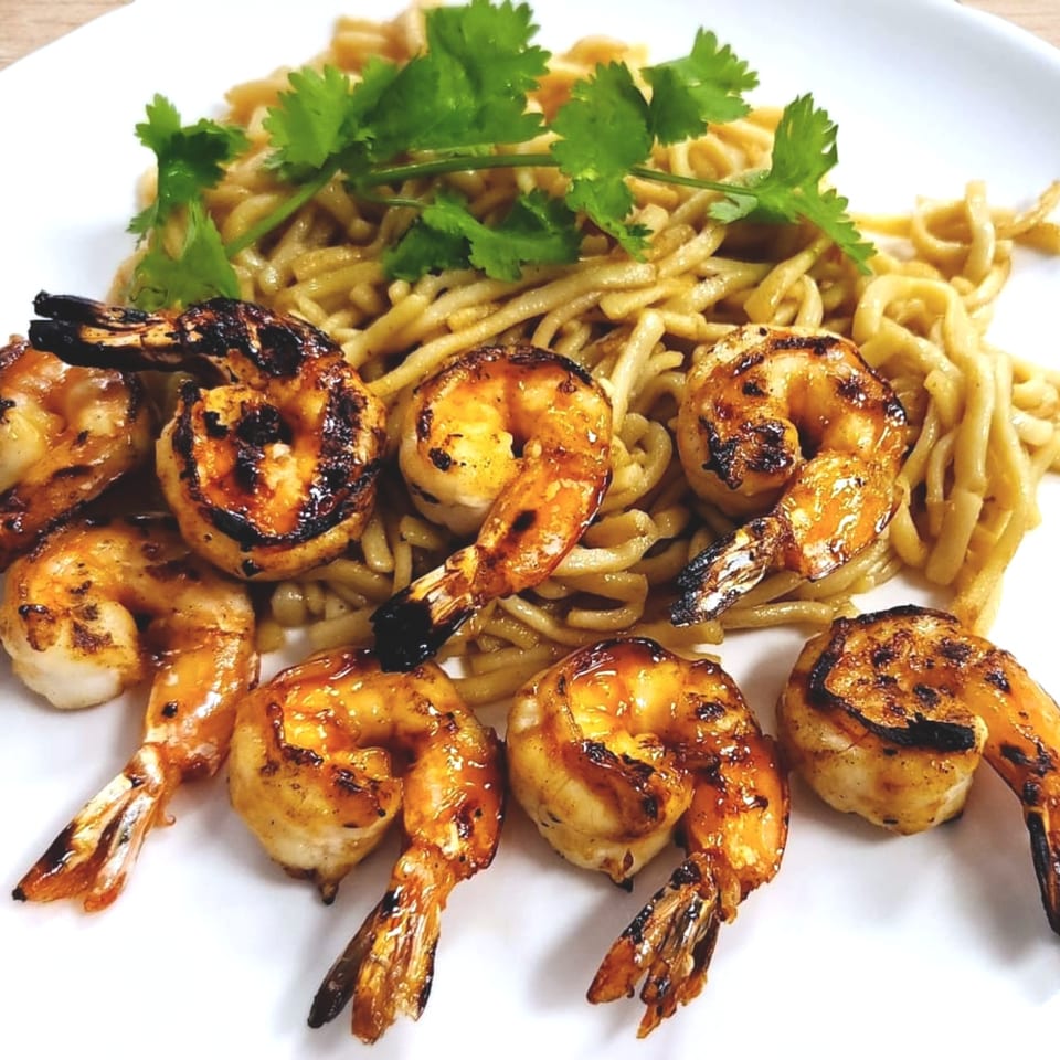 Grilled shrimp with charred marks and noodles topped with fresh cilantro on a white plate.