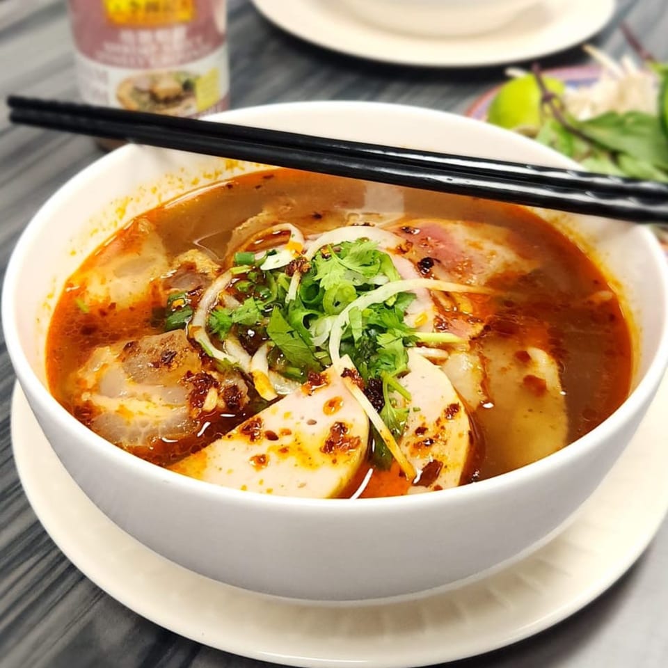 A vibrant bowl of Vietnamese Bun Bo Hue soup with chopsticks, garnished with herbs and lime.