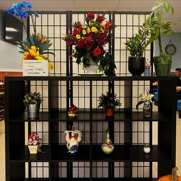 A black shelving unit with various floral arrangements and decorative items, in a Vietnamese restaurant.