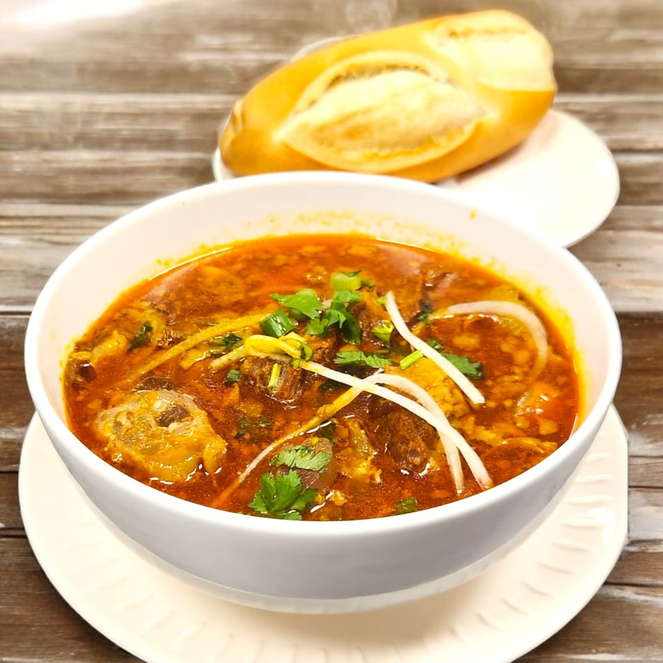 A bowl of Vietnamese beef stew (Bo Kho) with a side of banh mi bread on a wooden table.