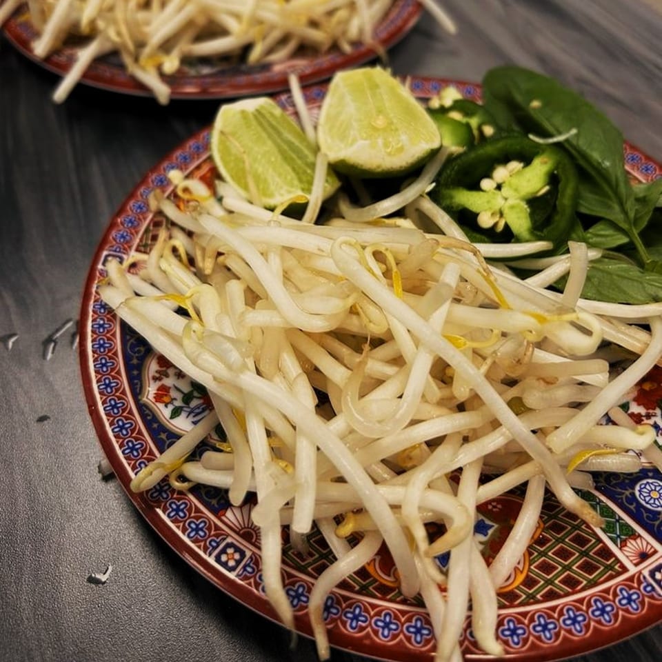 A plate of fresh bean sprouts, lime wedges, sliced jalapeños, and basil for Vietnamese pho.