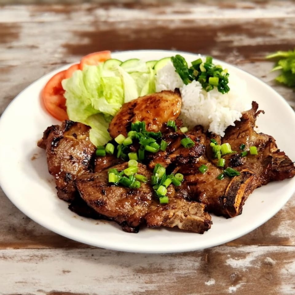 Vietnamese grilled pork chops with rice, lettuce, tomatoes, cucumbers, and green onions.