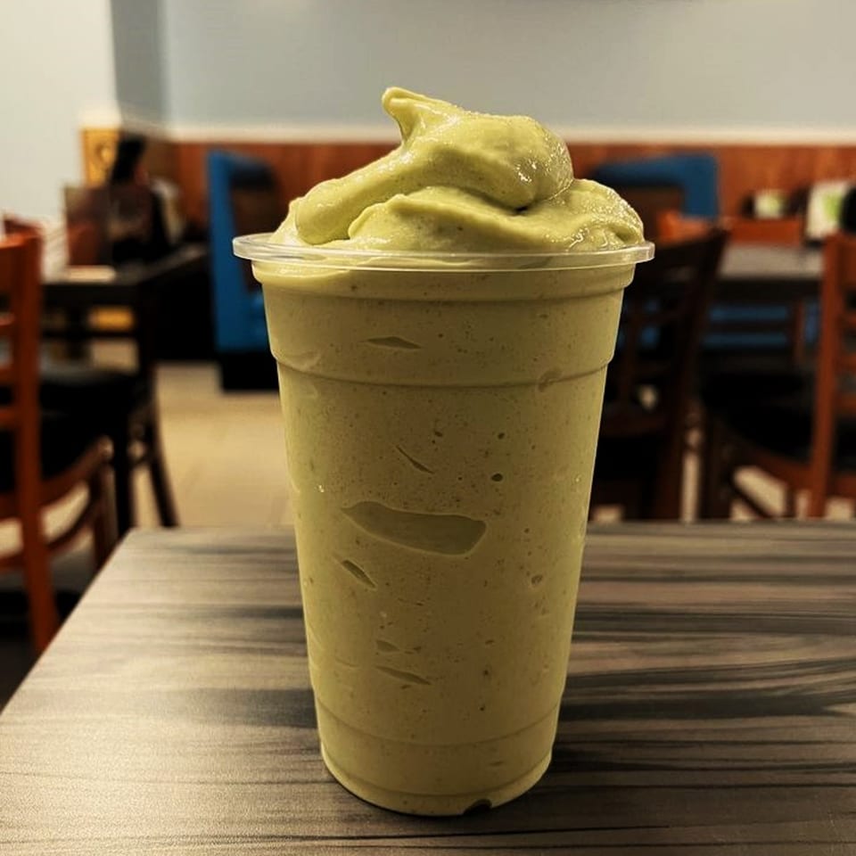 A green avocado smoothie with a dollop of whipped avocado on top, on a wooden table.