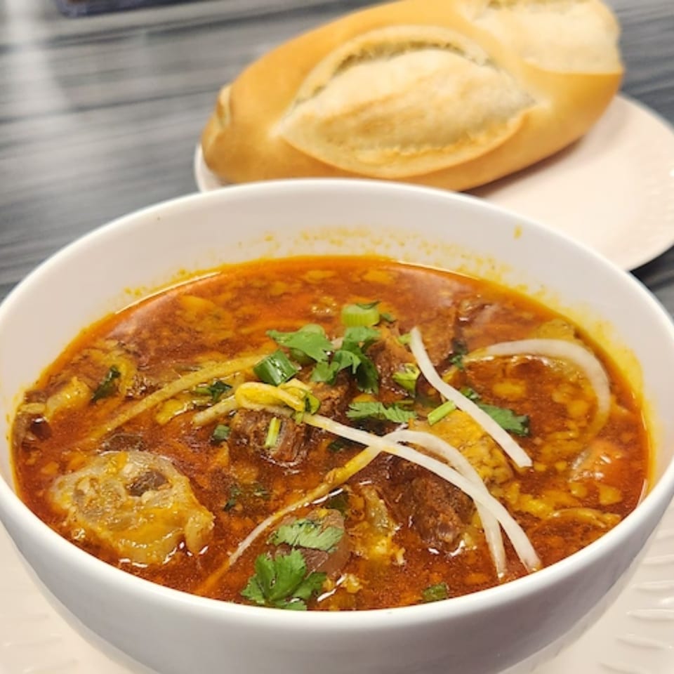 A bowl of Vietnamese beef stew with cilantro, onions, and a baguette on the side.