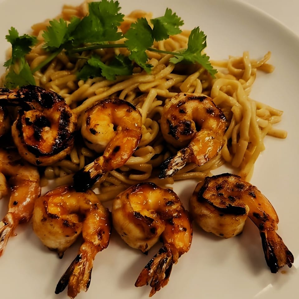 Grilled shrimp with char marks and noodles topped with fresh cilantro on a white plate.