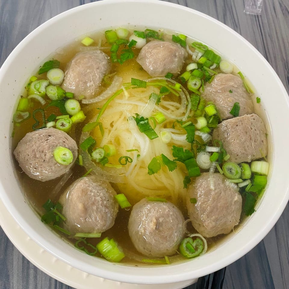 A bowl of Vietnamese pho with meatballs, noodles, and green onions in a clear broth.