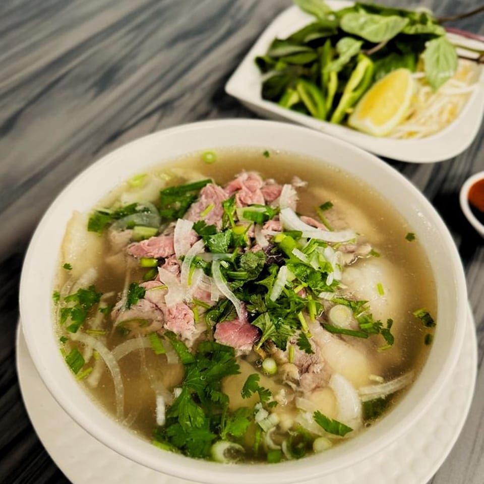 A bowl of Pho Huyen & Banh Mi's Vietnamese pho with beef, herbs, and a side of fresh garnishes.