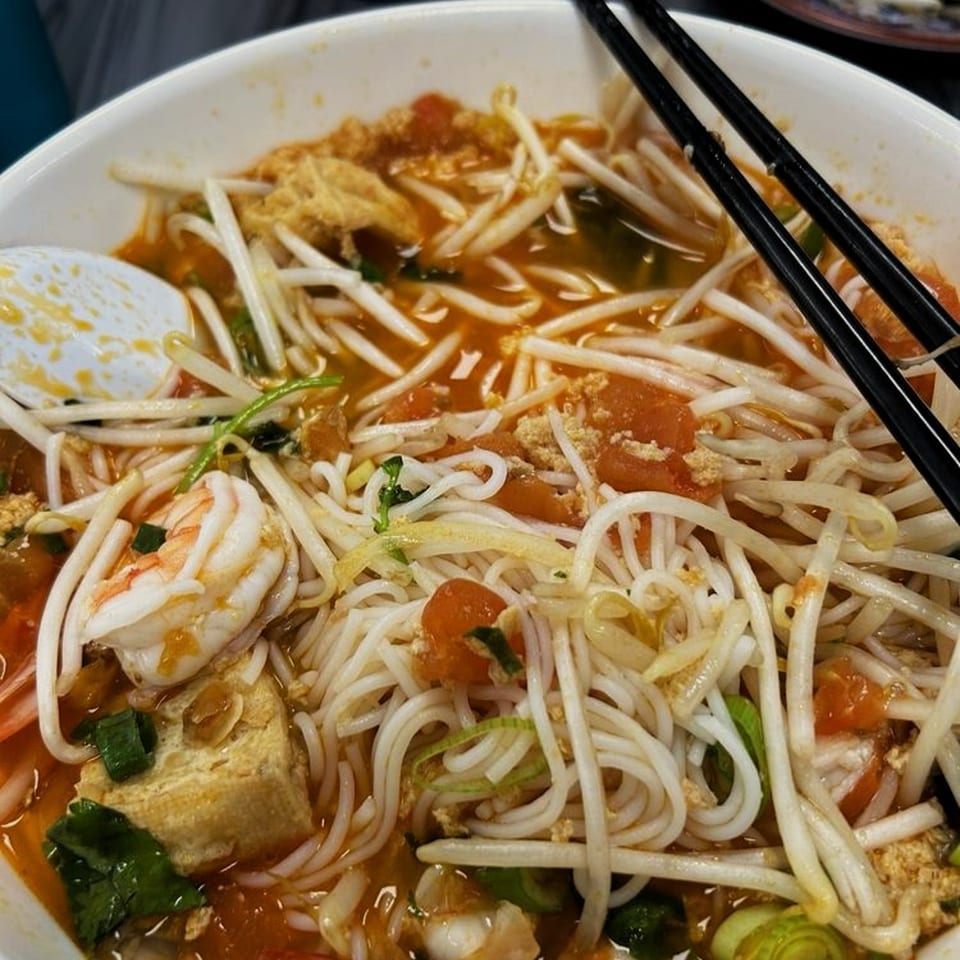 Close-up of a bowl of Vietnamese noodle soup with shrimp, tofu, bean sprouts, and chopsticks.