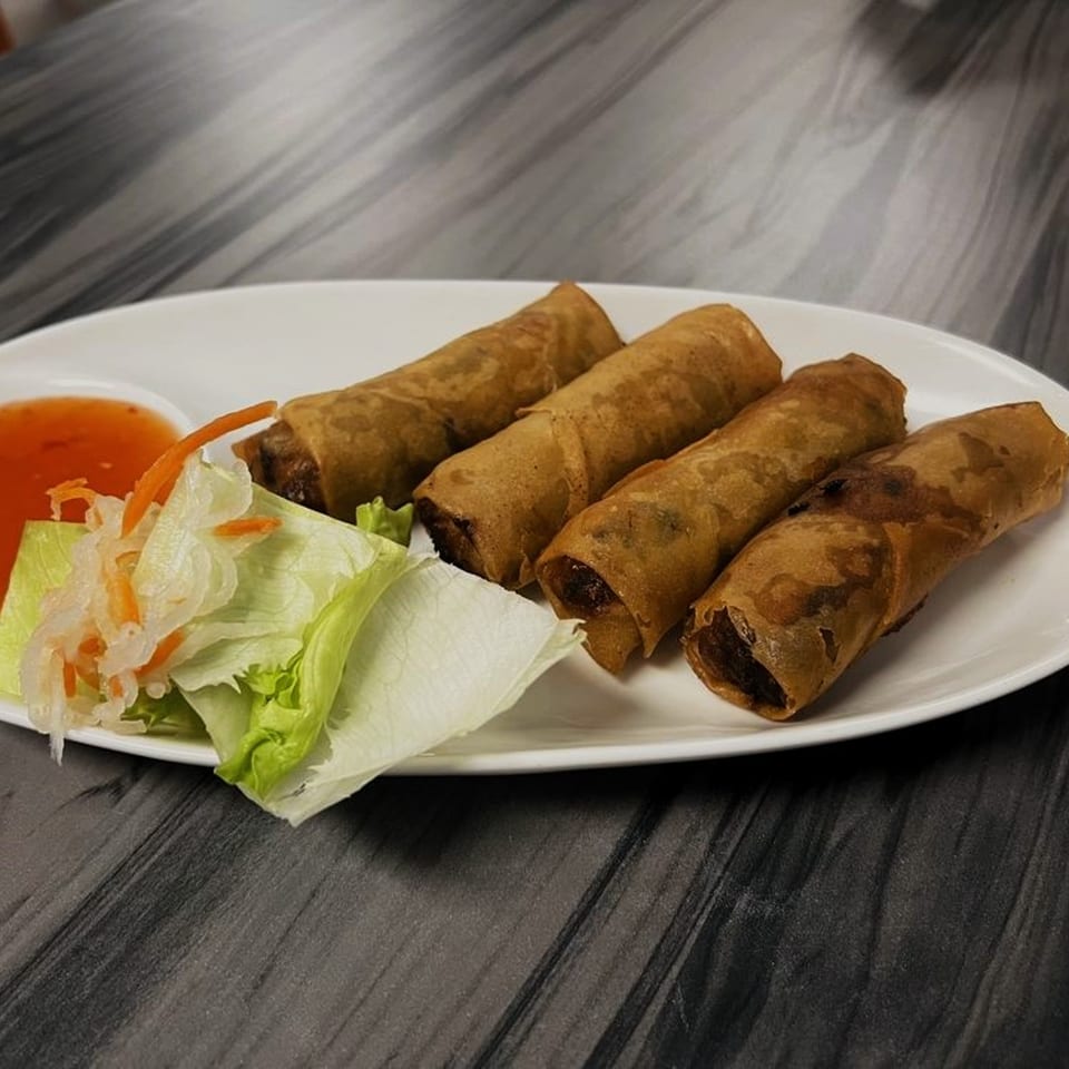 Four crispy Vietnamese spring rolls with lettuce, pickled vegetables, and sweet chili sauce on a white plate.