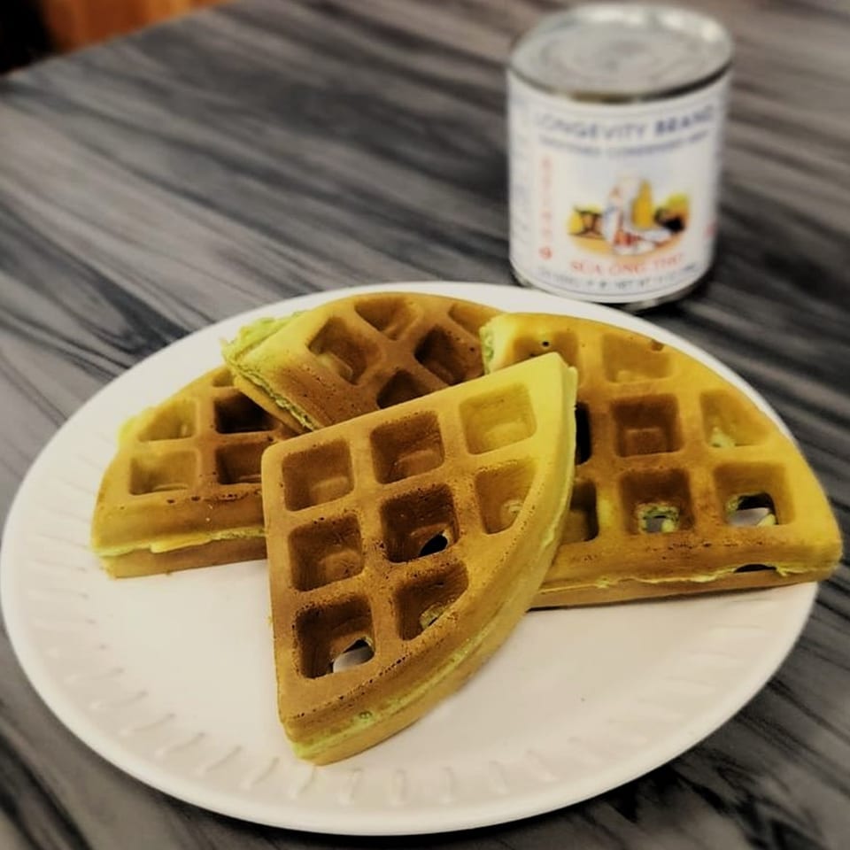 Golden-brown Vietnamese pandan waffles on a white plate with a can of condensed milk.